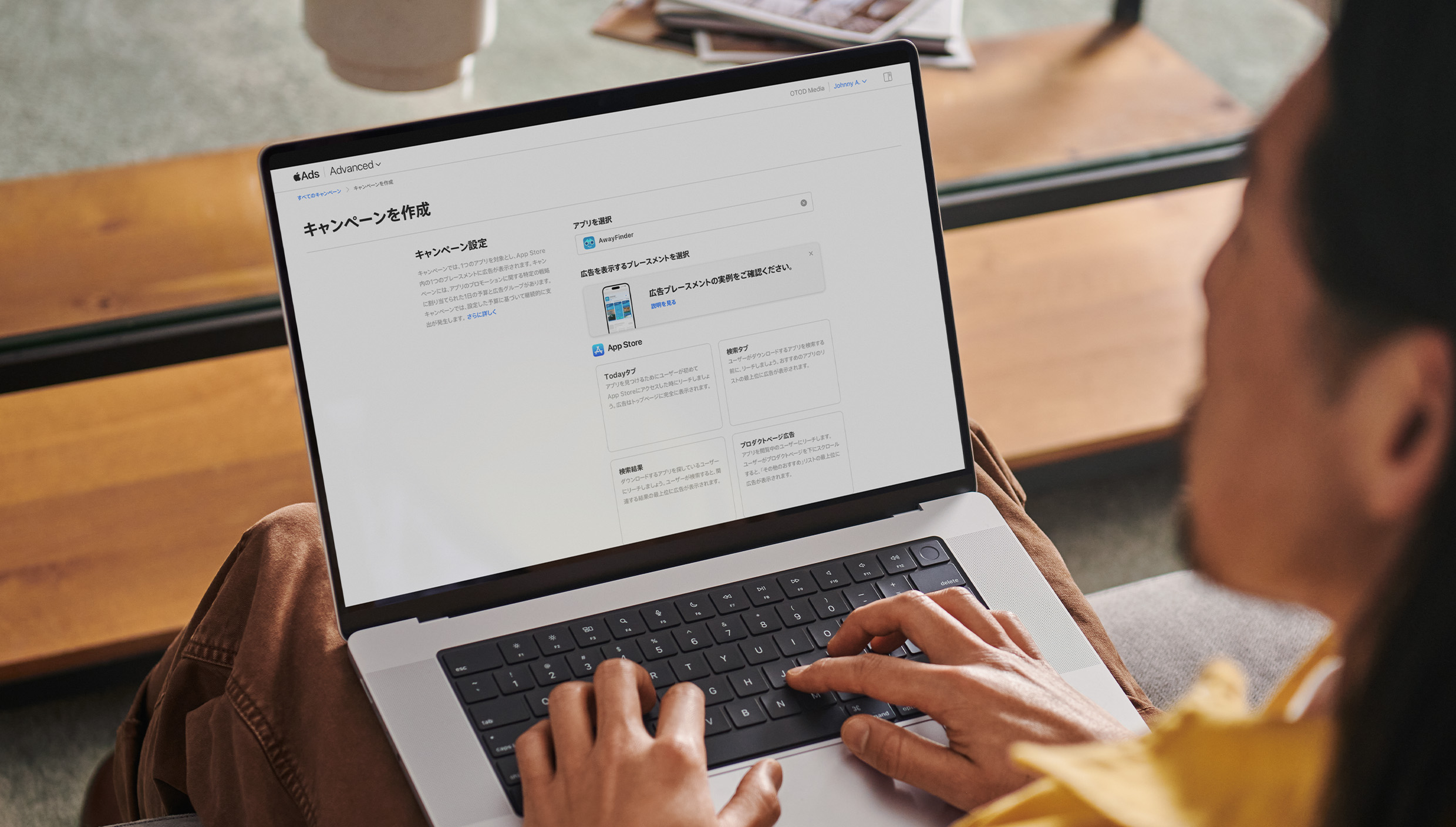 MacBookで作業している広告主。画面でApple Adsの「キャンペーンを作成」ページが開いており、利用可能なTodayタブ、検索タブ、検索結果、プロダクトページの4つの広告プレースメントが表示されている。